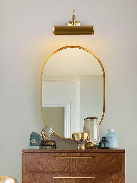 Brass tube lit above a mirror over a walnut dresser with small objects