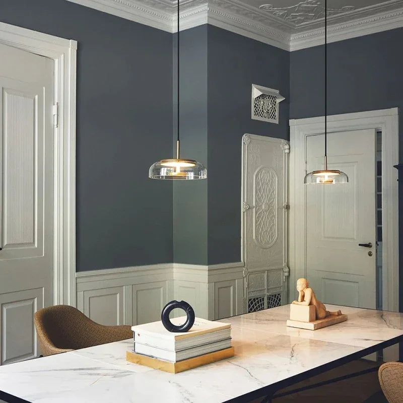 Two clear glass dome pendants hanging over a console table against a blue gray wall