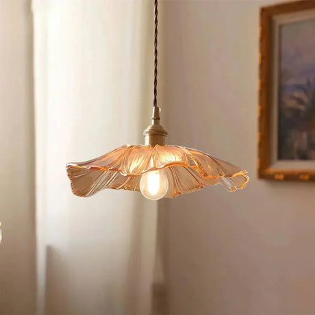 An amber lotus shade lit beside a framed landscape on a pale wall