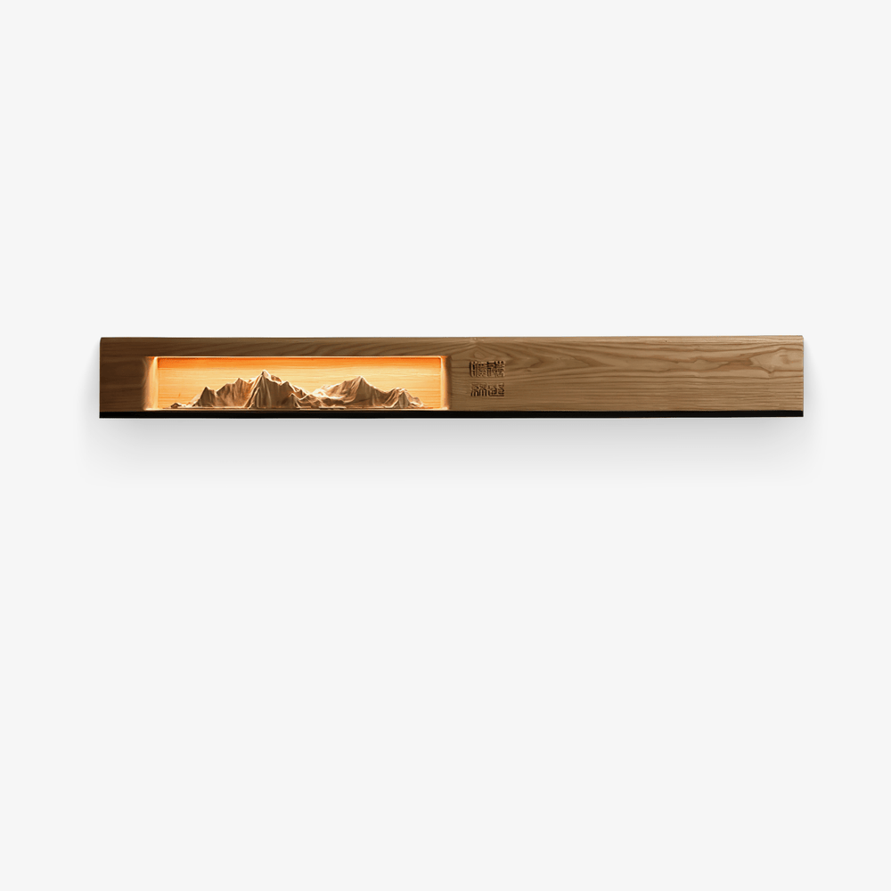 Long light wood wall panel with a lit carved mountain scene inside