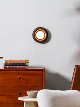 Sconce lit on a wall above books on a teak dresser next to a soft chair