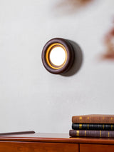 Sconce lit close above the top of a teak dresser holding stacked books