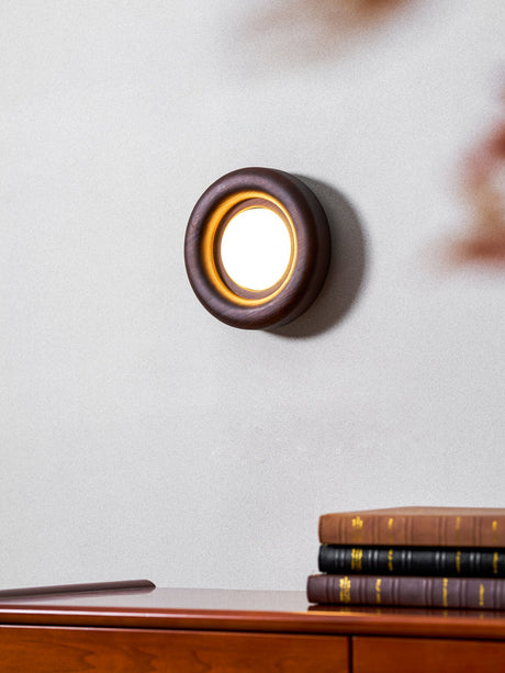 Sconce lit close above the top of a teak dresser holding stacked books