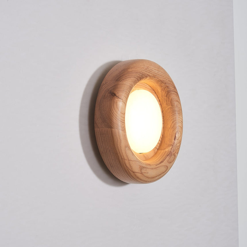 Light wood ring lit warm, the round diffuser sitting inside the rounded rim