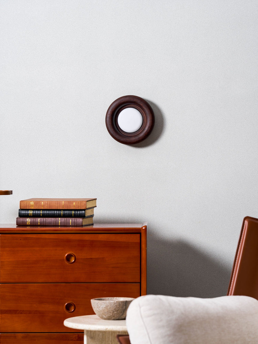 Sconce unlit on a wall above a teak dresser beside a chair and a side table