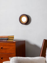 Sconce lit above a teak dresser beside a pale armchair with a cushion