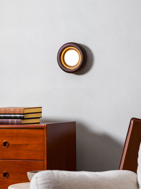 Sconce lit above a teak dresser beside a pale armchair with a cushion