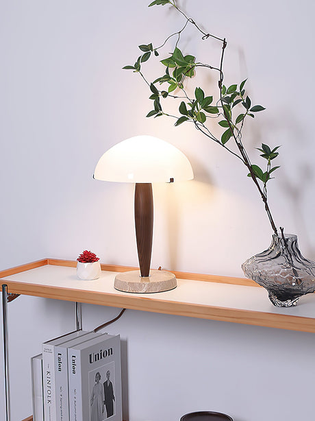 Marble base table lamp lit on a narrow wall shelf beside a vase