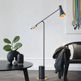 The lit lamp reaching over a black table with a vase and a plant in a pale room