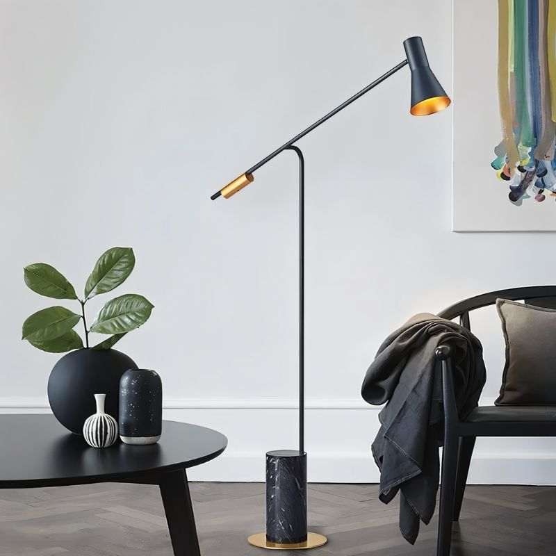 The lit lamp reaching over a black table with a vase and a plant in a pale room