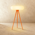 An orange wood tripod carrying a wide rounded capsule shade lit from within