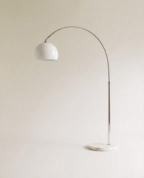A curved chrome arm carrying a white glass dome above a round white marble base
