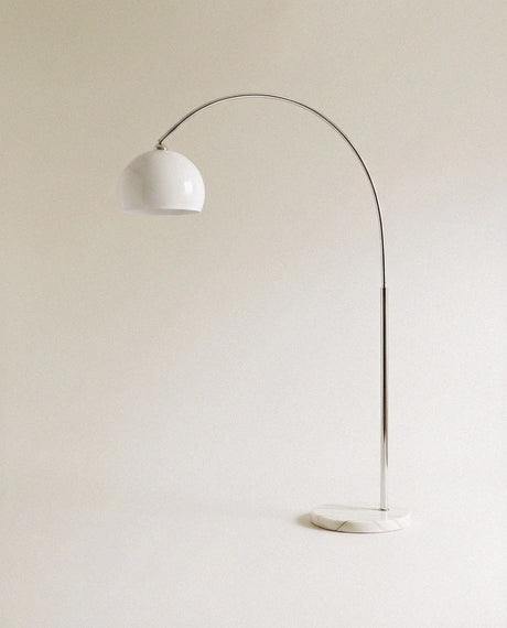 A curved chrome arm carrying a white glass dome above a round white marble base