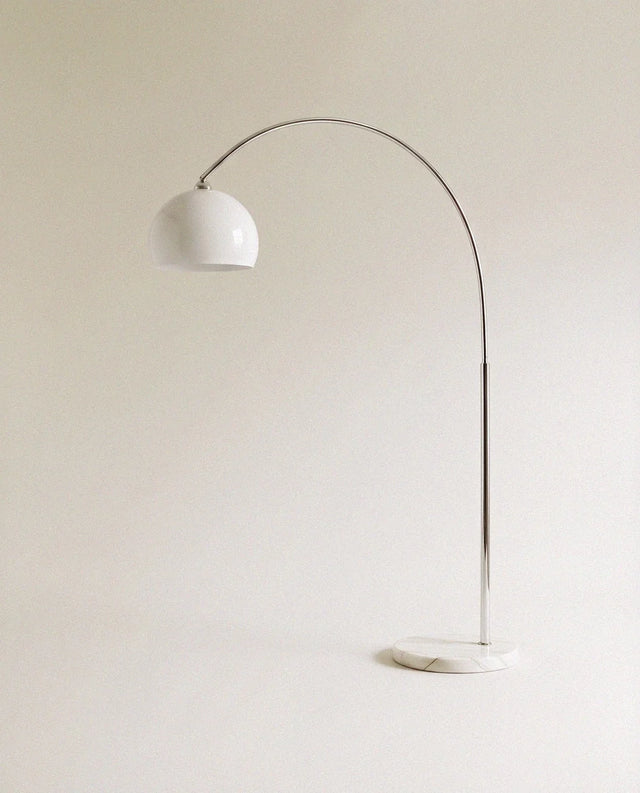A curved chrome arm carrying a white glass dome above a round white marble base