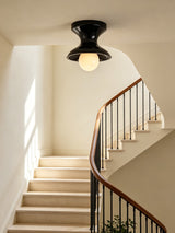 Navy spool ceiling light above a curving staircase with a wrought iron rail