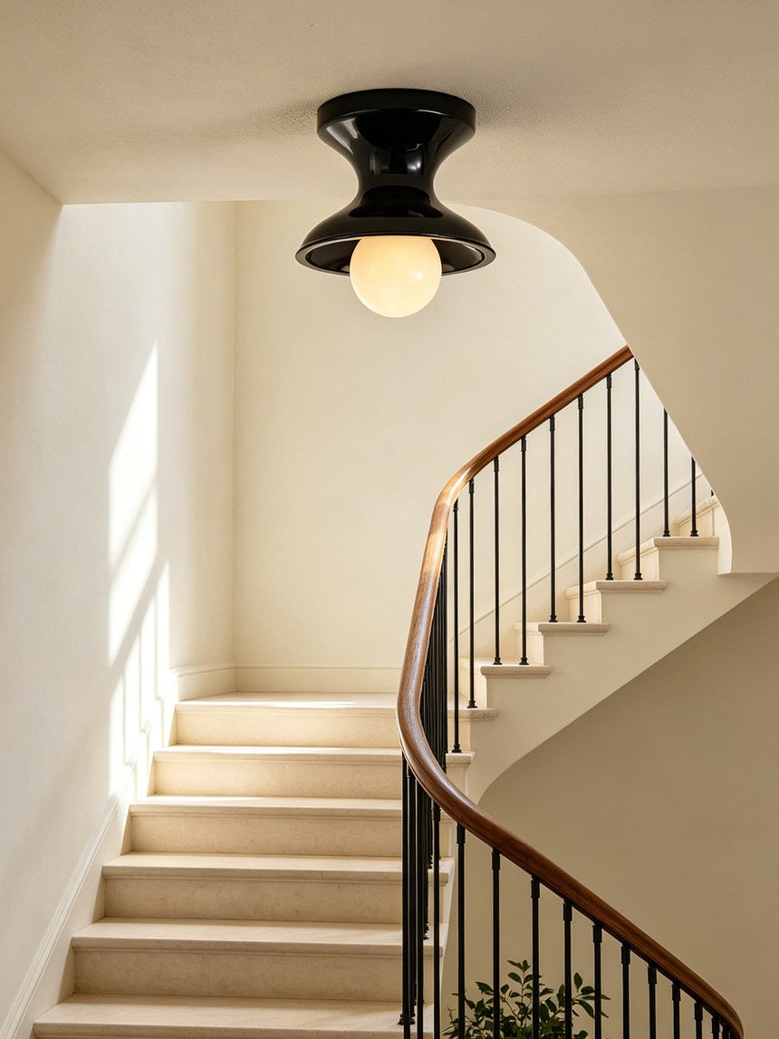 Navy spool ceiling light above a curving staircase with a wrought iron rail
