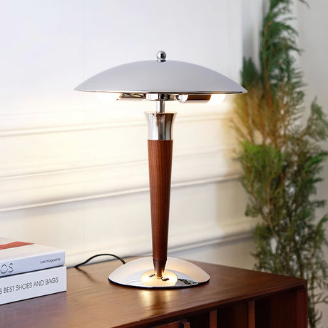 Chrome dome table lamp lit on a console stacked with books