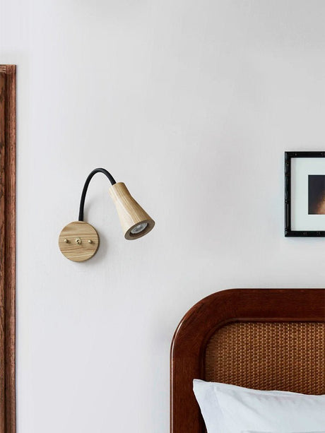 Sconce lit on a white wall beside a cane headboard and a framed print