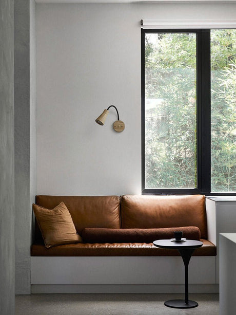 Sconce on a wall above a window bench with a leather seat and cushion