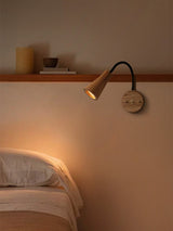 Light wood sconce lit above a bed beside a narrow wall shelf