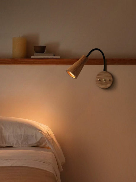 Light wood sconce lit above a bed beside a narrow wall shelf