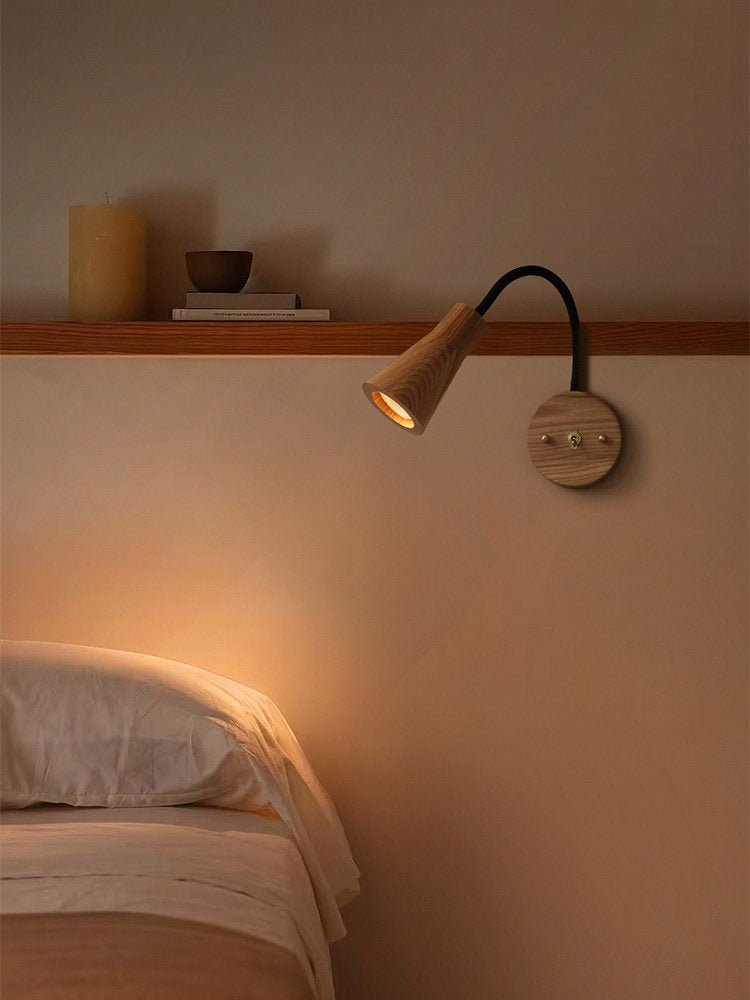 Light wood sconce lit above a bed beside a narrow wall shelf
