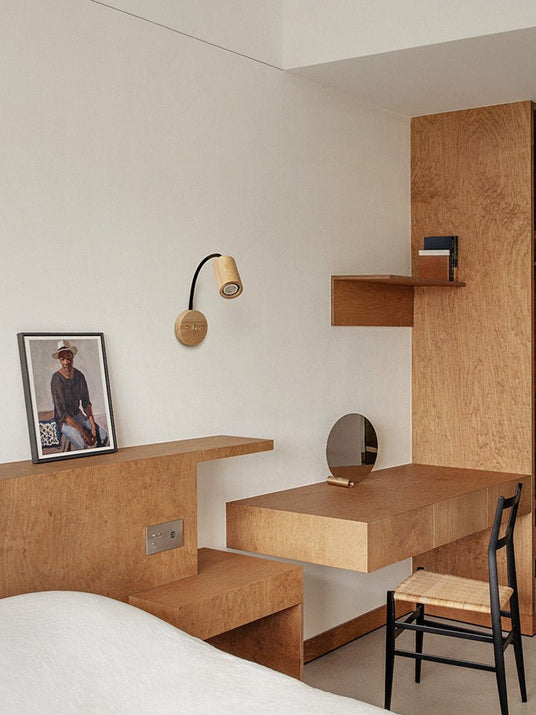 Sconce lit above a built in plywood desk beside a bed and a mirror
