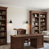 Sconces lit in a study beside a bookcase, a leather chair and a desk