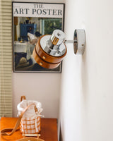 Sconce lit beside a poster above a console with a checked cloth and a jug