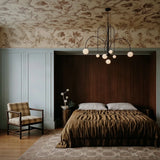 The black version lit over a bed against a paneled wall and floral wallpaper