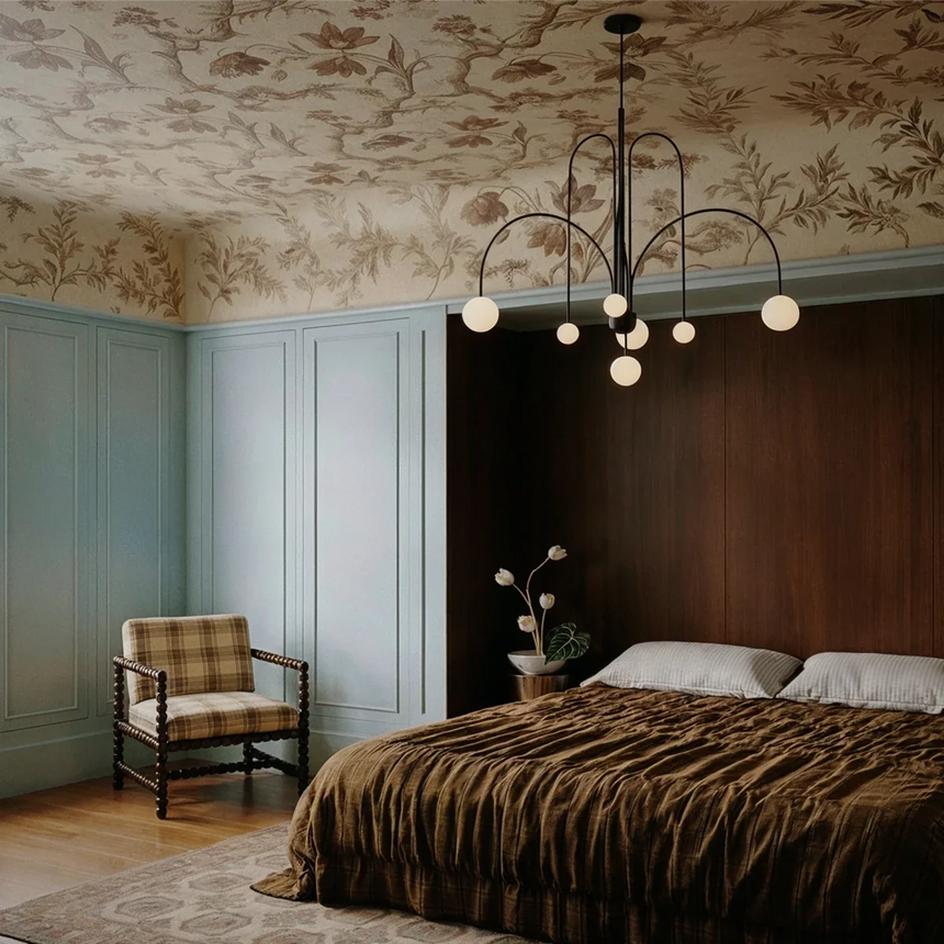 The black version above a bed with an armchair in a room with floral wallpaper