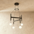 The same crossed bar frame in black wood carrying four lit milk glass globes