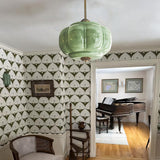 Green ribbed shade lit in a room with patterned wallpaper and a piano beyond