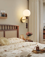 Milk glass globe lit on a wall above a cane headboard and a flower vase