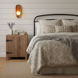 Sconce lit on a plank bedroom wall above a wood dresser beside a bed