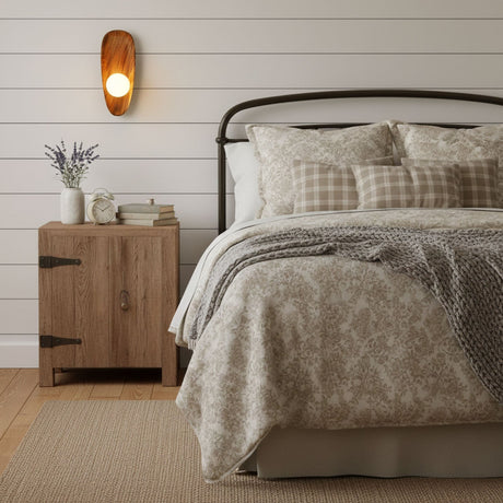 Sconce lit on a plank bedroom wall above a wood dresser beside a bed