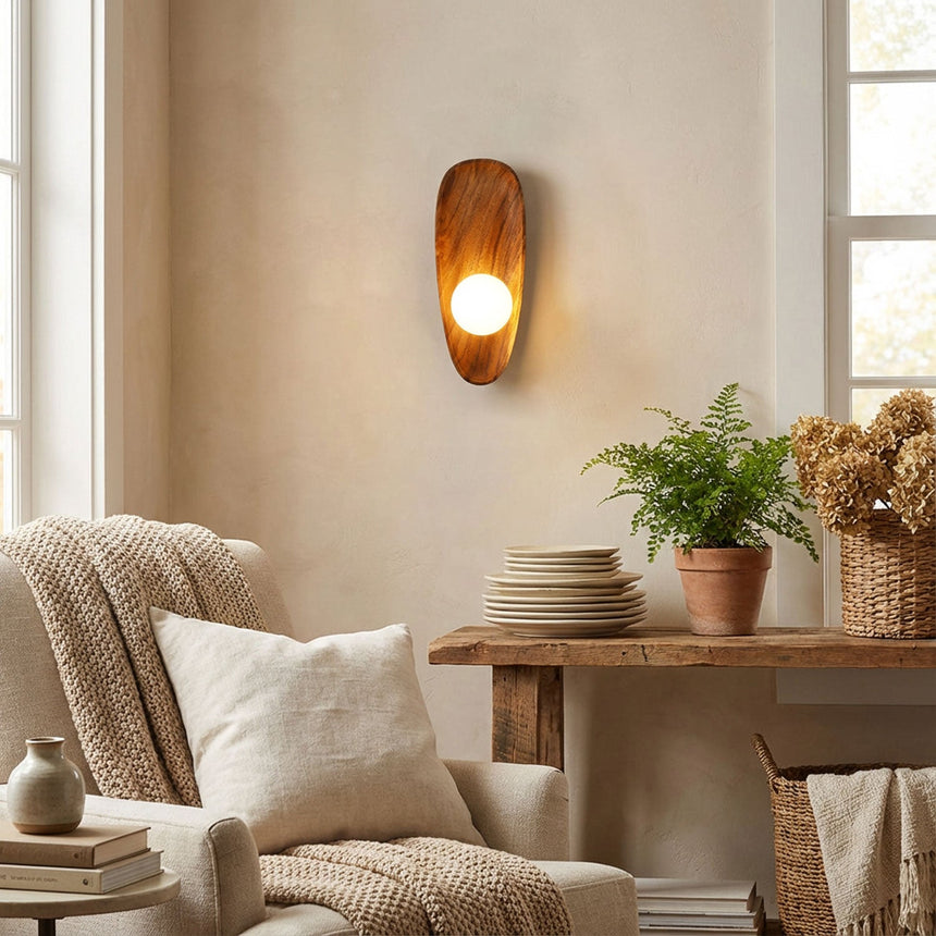Sconce lit above a console stacked with plates beside a plant and a chair