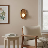 Sconce lit above a side table with books beside a pale armchair and a window