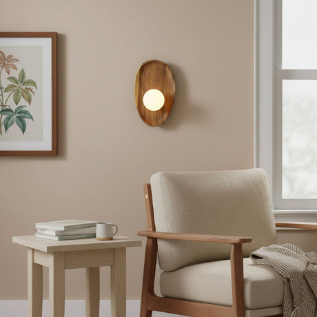Sconce lit above a side table with books beside a pale armchair and a window