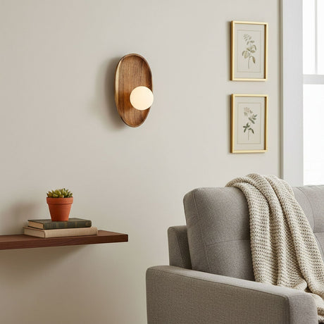 Sconce lit beside framed prints above a shelf holding books and a plant