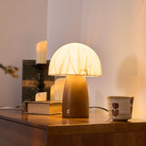 Mini table lamp lit on a wooden sideboard beside candles and a book