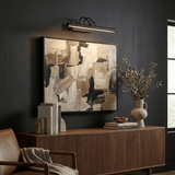 Black bar lit above an abstract canvas over a walnut sideboard on a dark wall