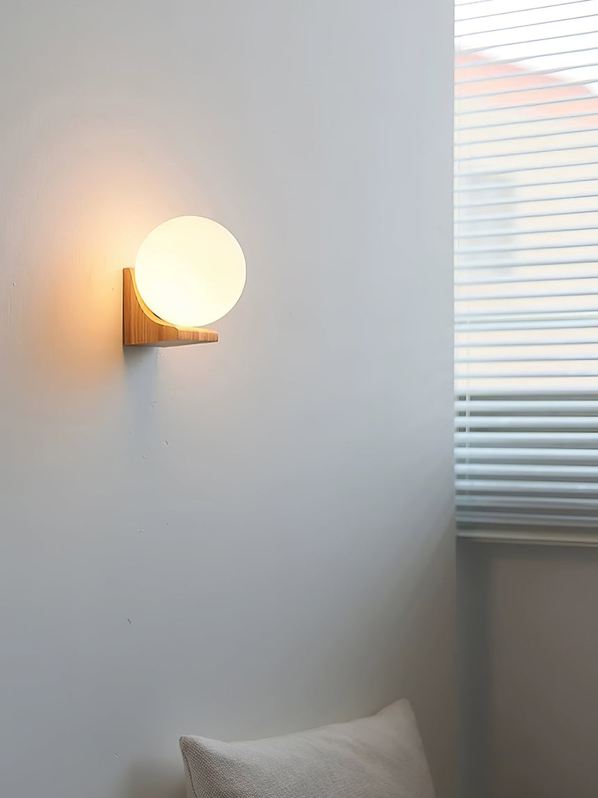 Sconce lit above a pillow beside a window with light through the blind