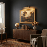 Gold bar lit above a framed painting over a walnut console with books and a vase