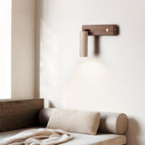 Sconce lit above a bed with a bolster cushion and a folded knit throw