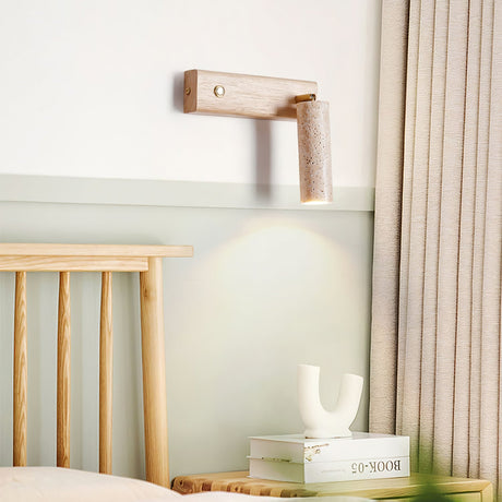 Sconce lit in a bedroom corner beside a slatted headboard and stacked books