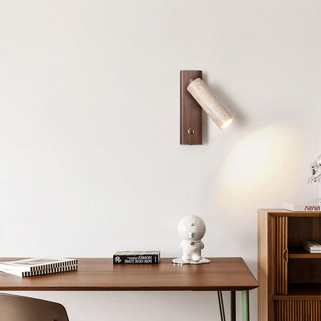 Sconce lit above a walnut desk with books, a notebook and a small sculpture