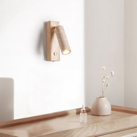 Sconce lit above a pale wood desk holding a vase of dried stems and a dish