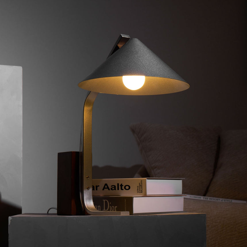 Minimalist desk lamp lit in a dark room over a stack of books