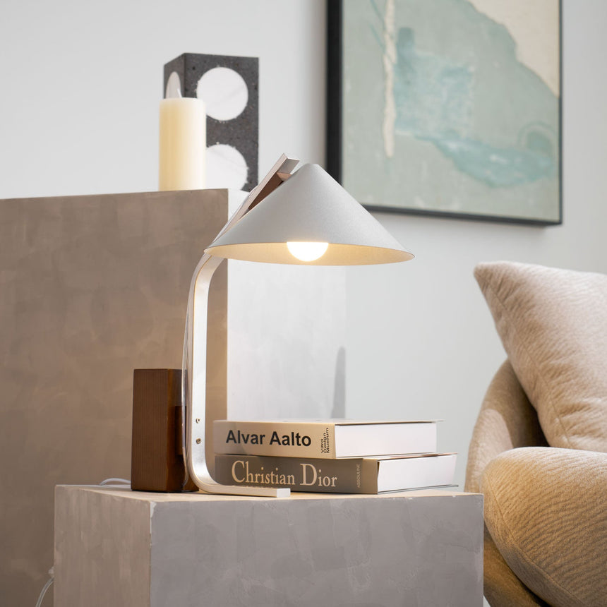 Minimalist desk lamp lit on a plinth beside a stack of books